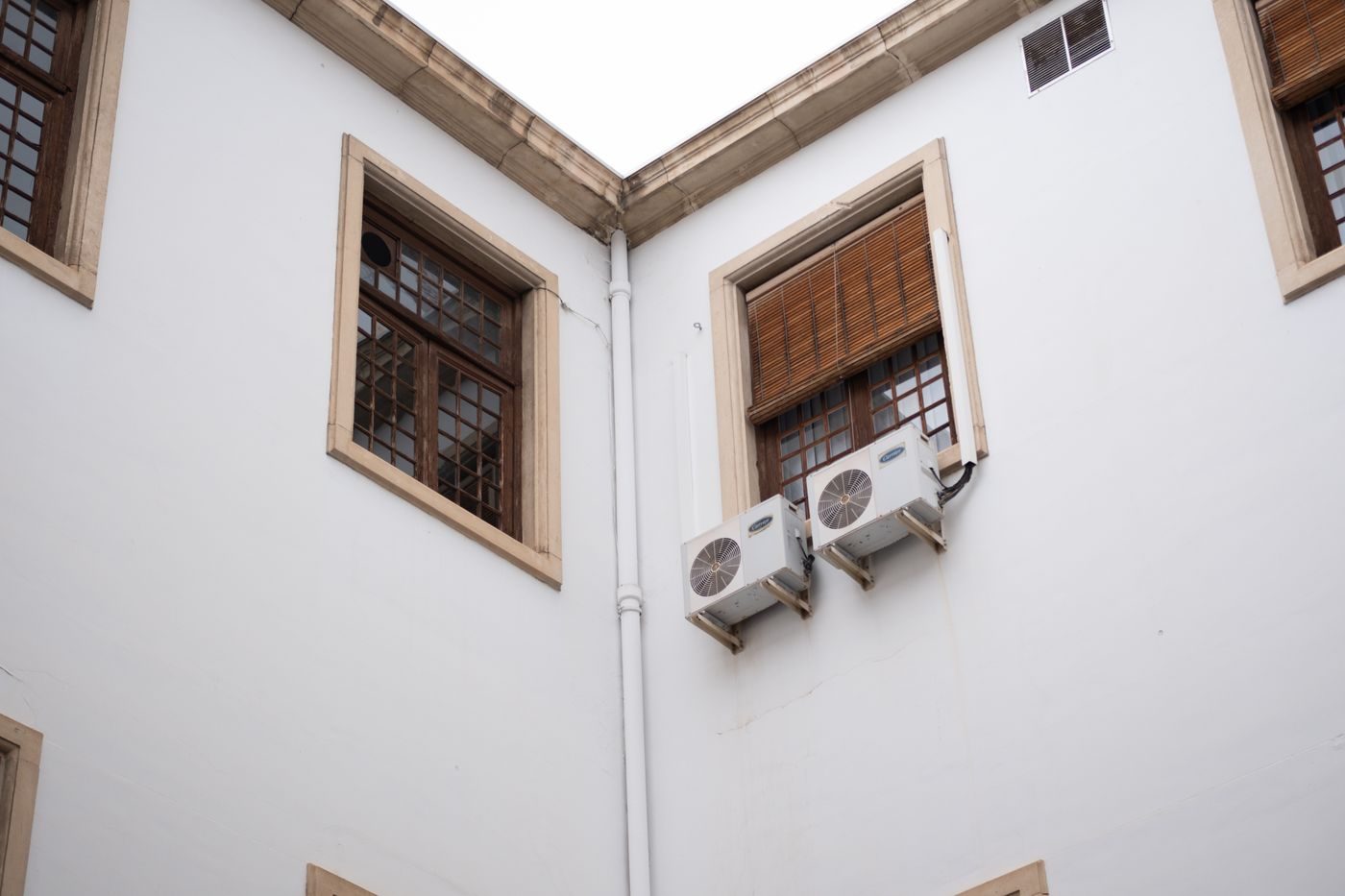 Two air conditioning outdoor units fixed under windows on a white rendered building