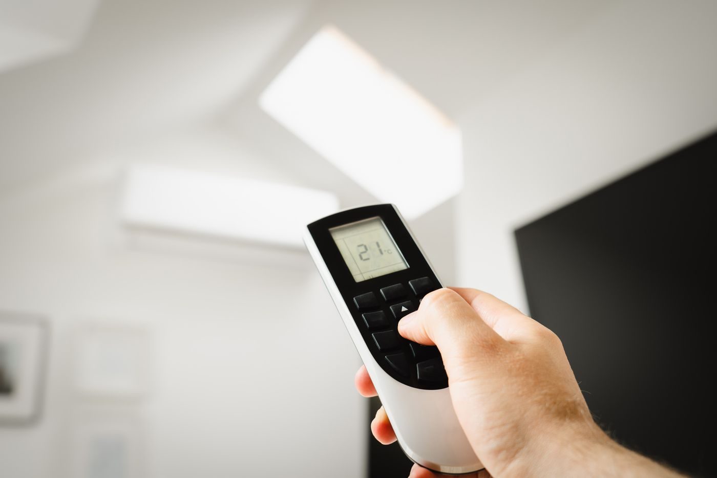 Hand pointing a remote control at a wall mounted split air conditioning unit